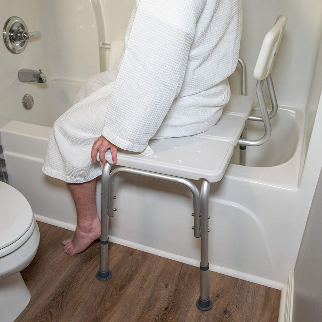 A person in a white bathrobe sitting on a bathtub transfer bench in a bathroom.