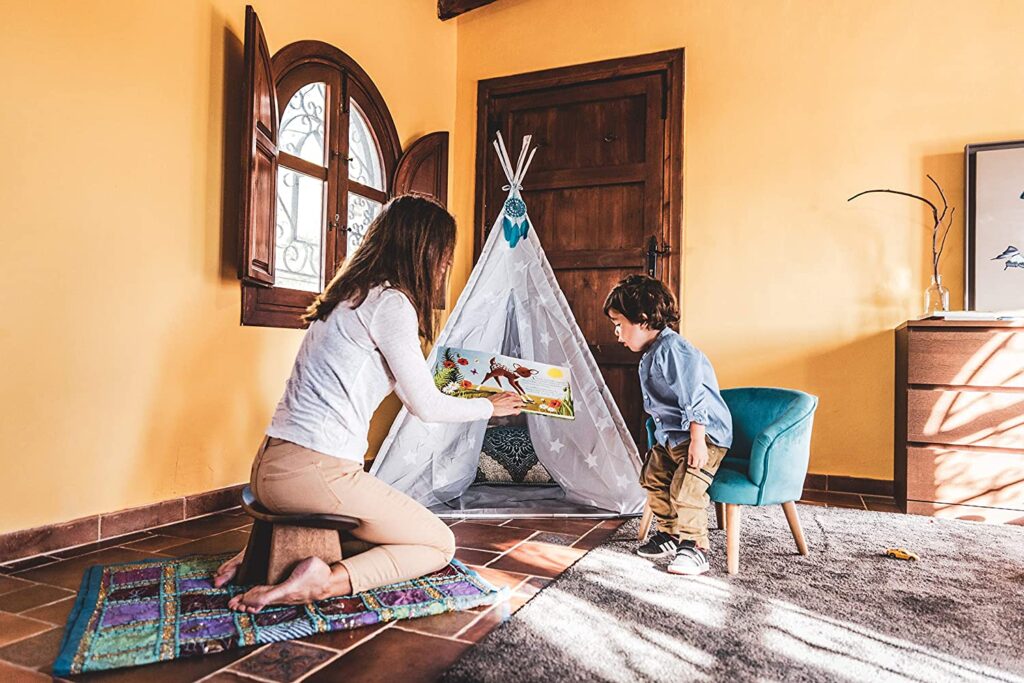 Mother reading a storybook to her young son in a cozy room with a teepee play tent.