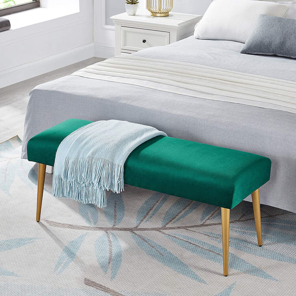 Green upholstered bench with gold legs at the foot of a bed in a modern bedroom.