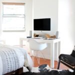 Bright and modern bedroom workspace with an iMac on a white desk, an ergonomic chair, and New York-themed decor.