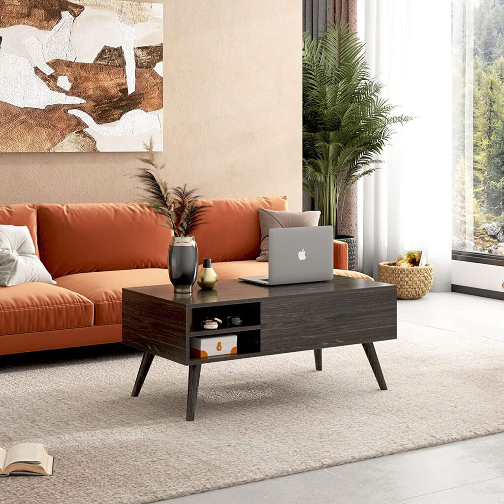 Modern living room with an orange sofa, wooden coffee table, laptop, and decorative items, with a large plant and artwork in the background.