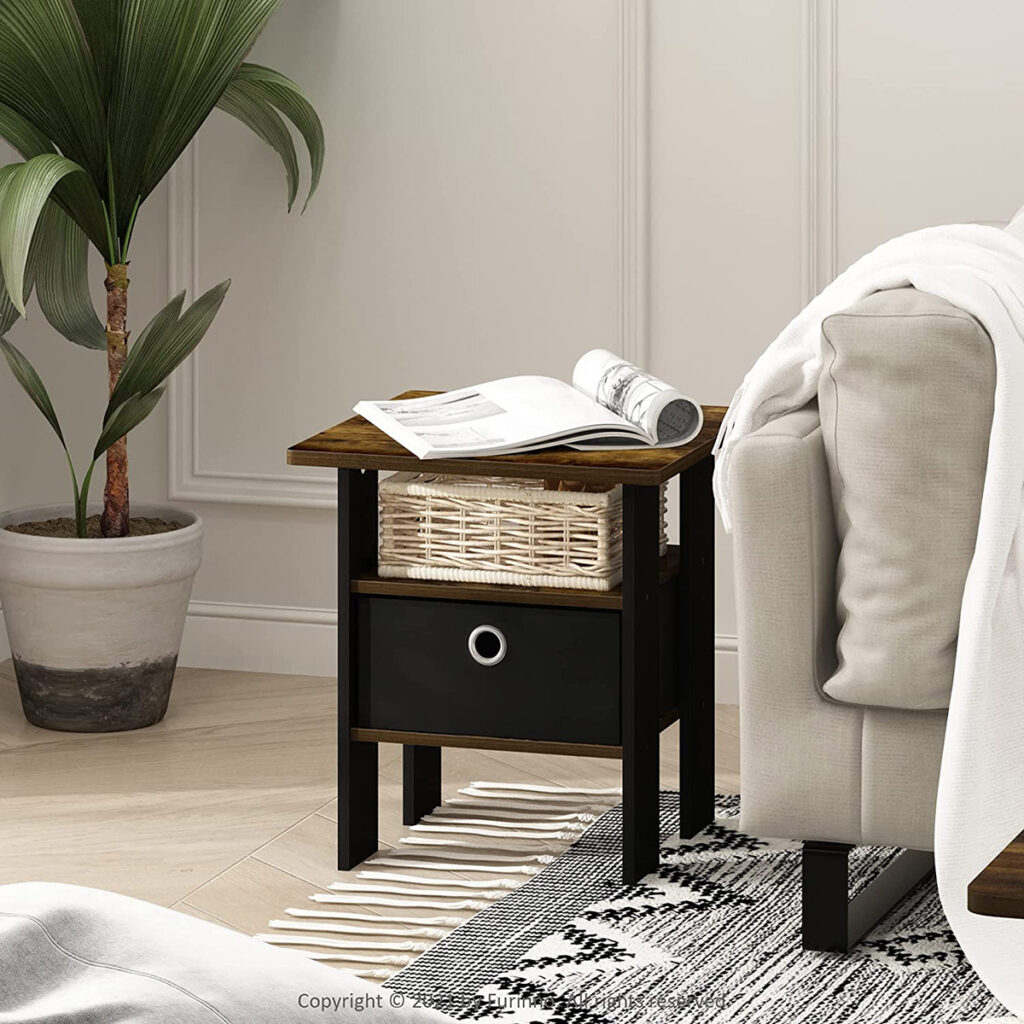 Modern side table with wooden top, wicker basket, and drawer, placed next to a sofa with a potted plant in the background.