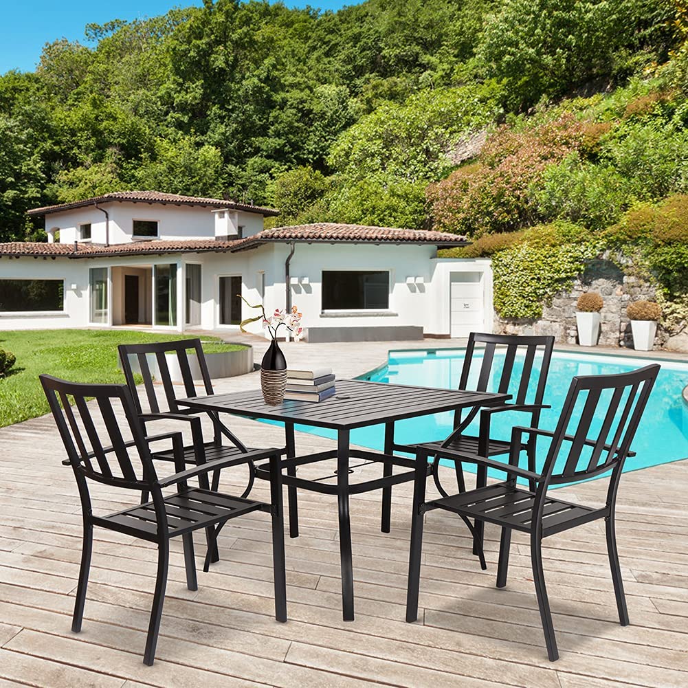 Outdoor patio dining set with black metal chairs and table beside a swimming pool and modern house.